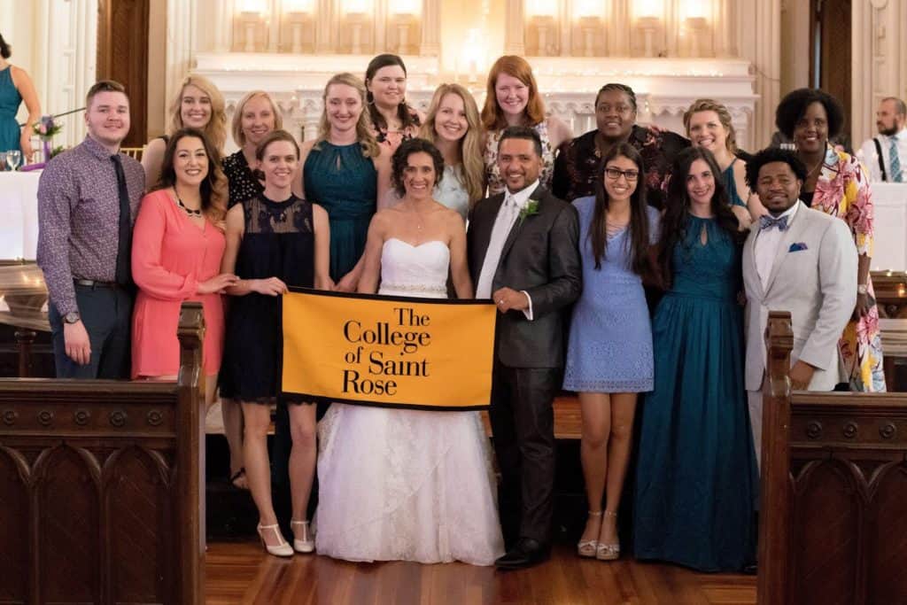 Rachel Deeb Gutierrez ’02, G’04 sent a lovely photo of Saint Rose alums who attended her wedding to Victor Gutierrez in June 2018, at her wedding with Saint Rose alums and Saint Rose banner
