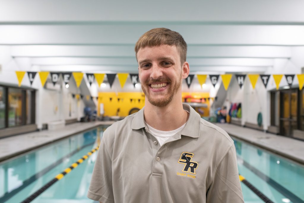 Kevin Walsh standing in front of the Saint Rose pool with gold and black triangle flags hanging behind him.